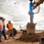 3 män tittat på när en jordborr gräver sig ner i marken.