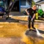 En man spolar rent gårdsplanen av asfalt med en hydrauildriven högtrycksvattenpump.