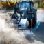 En traktor utrustad med spolrör tvättar en landsväg.