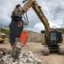 En gul CAT grävmaskin med en pulveriserare krossar stora betongblock.
