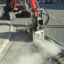 En grävmaskiner fräser asfalt intill en trottoar.