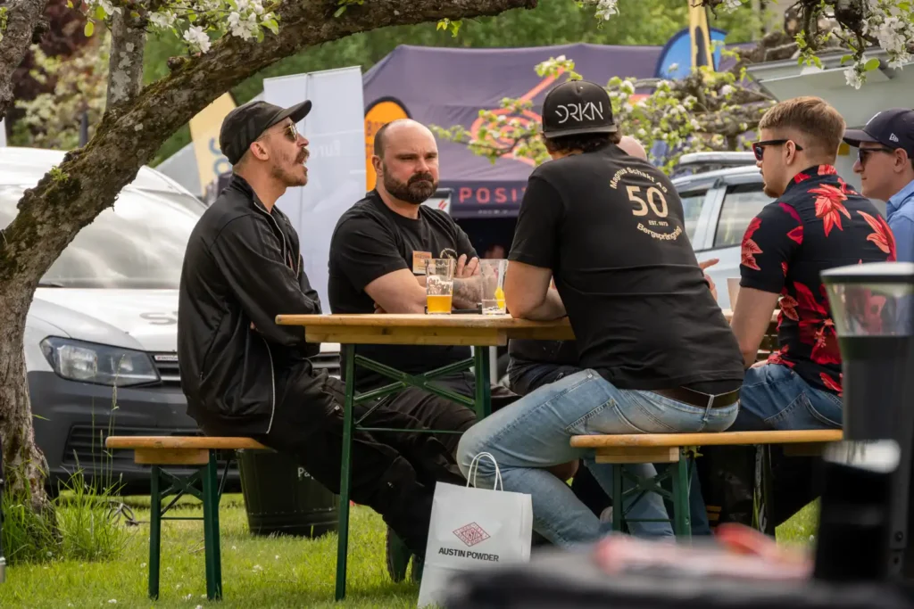 Ett gäng grabbar svalkar sig i skuggan under ett träd och dricker öl på Mässan Borr & Spräng i Bålsta 2023.