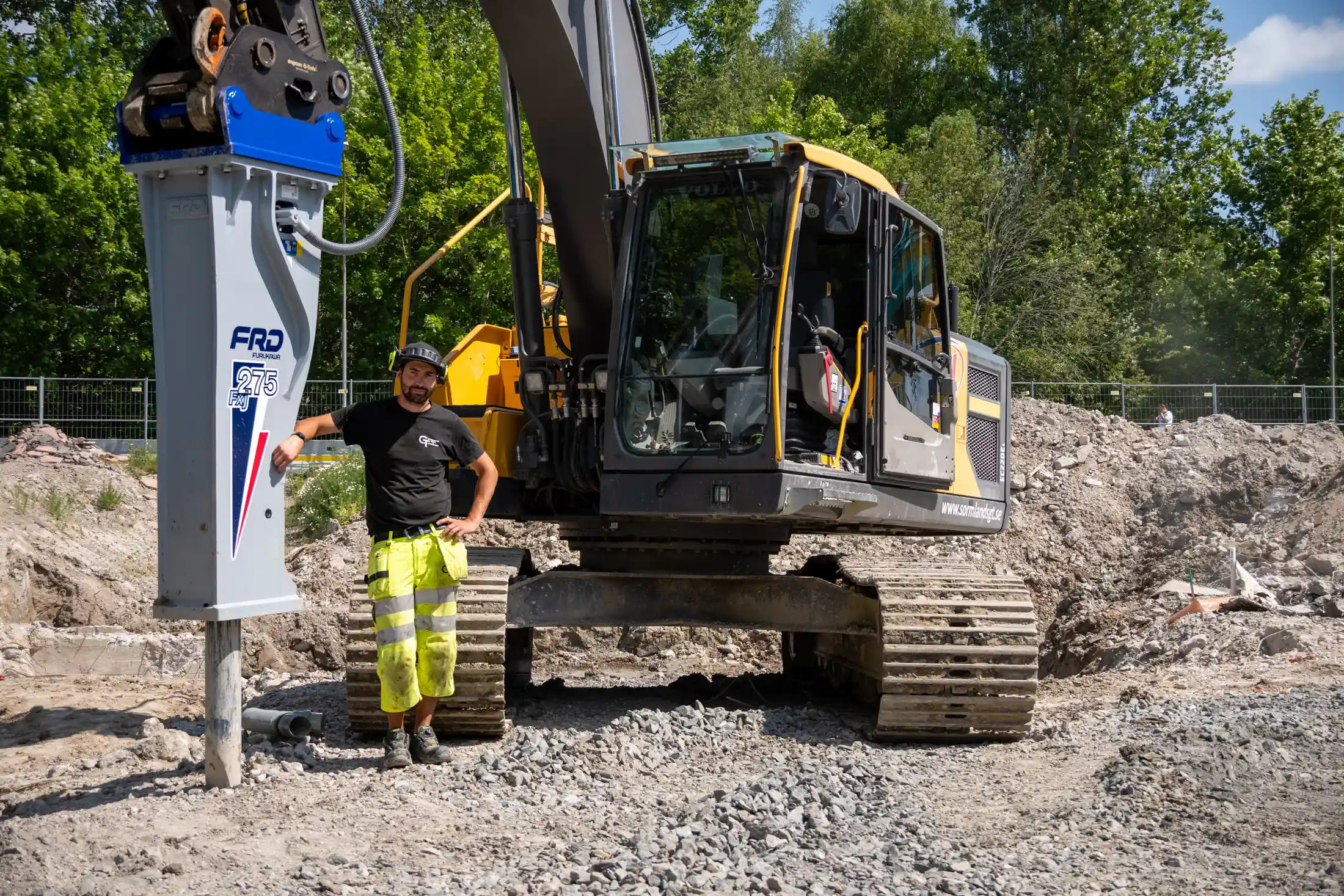 En Volvo EC220EL i Nyköping Bredvid står grävmaskinisten bredvid en hydraulhammare som är monterad på grävmaskinen