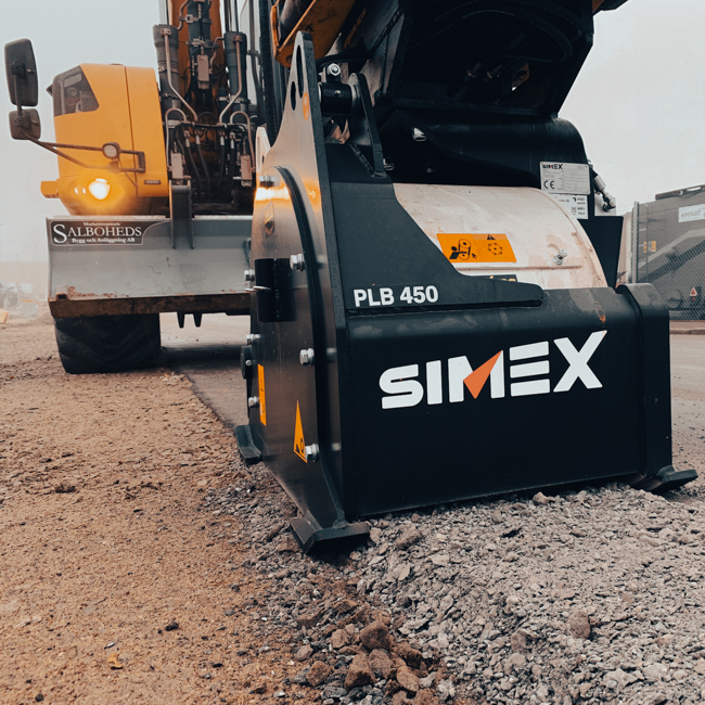 Närbild av en SIMEX fräs monterad på en grävmaskin i färd med att bearbeta asfalterad yta på en byggarbetsplats