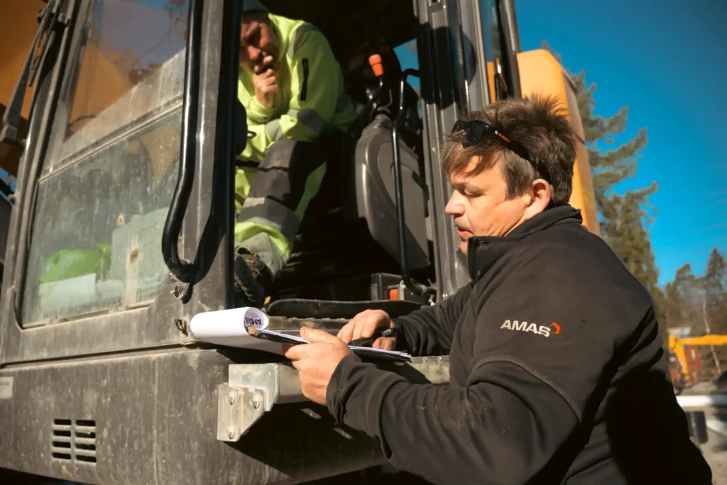 AMAS tekniker går igenom dokumentation med förare i en Case CX245D SR grävmaskin.