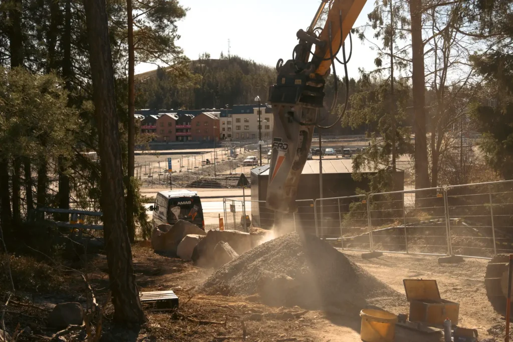 Hydraulhammare i arbete med grus och byggarbetsplats i bakgrunden, Väsjön, Sollentuna.