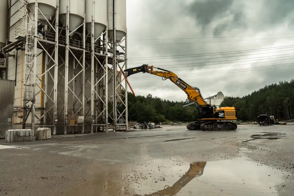 Grävmaskin med stålsax arbetar vid rivning av betongfabrik.