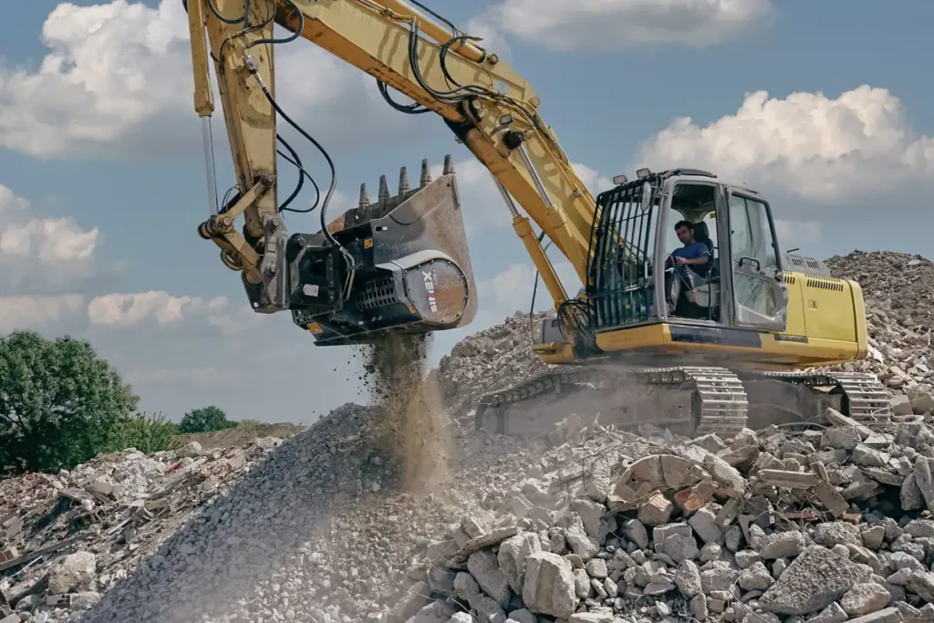 Grävmaskin utrustad med Simex CBE malningsskopa som finfördelar betongmassor på återvinningsplats.