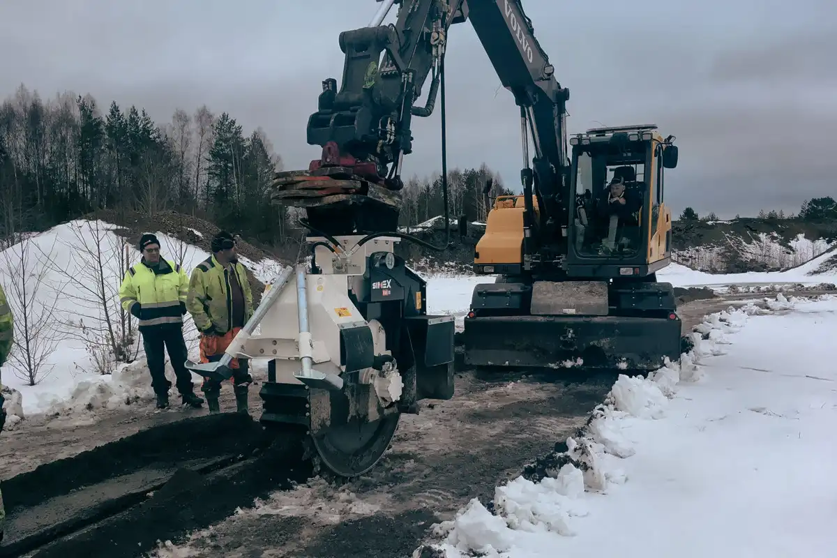 Simex hjulsåg i arbete på Volvo-grävmaskin som utför spårsågning i asfalt på snötäckt väg vid fältarbete.