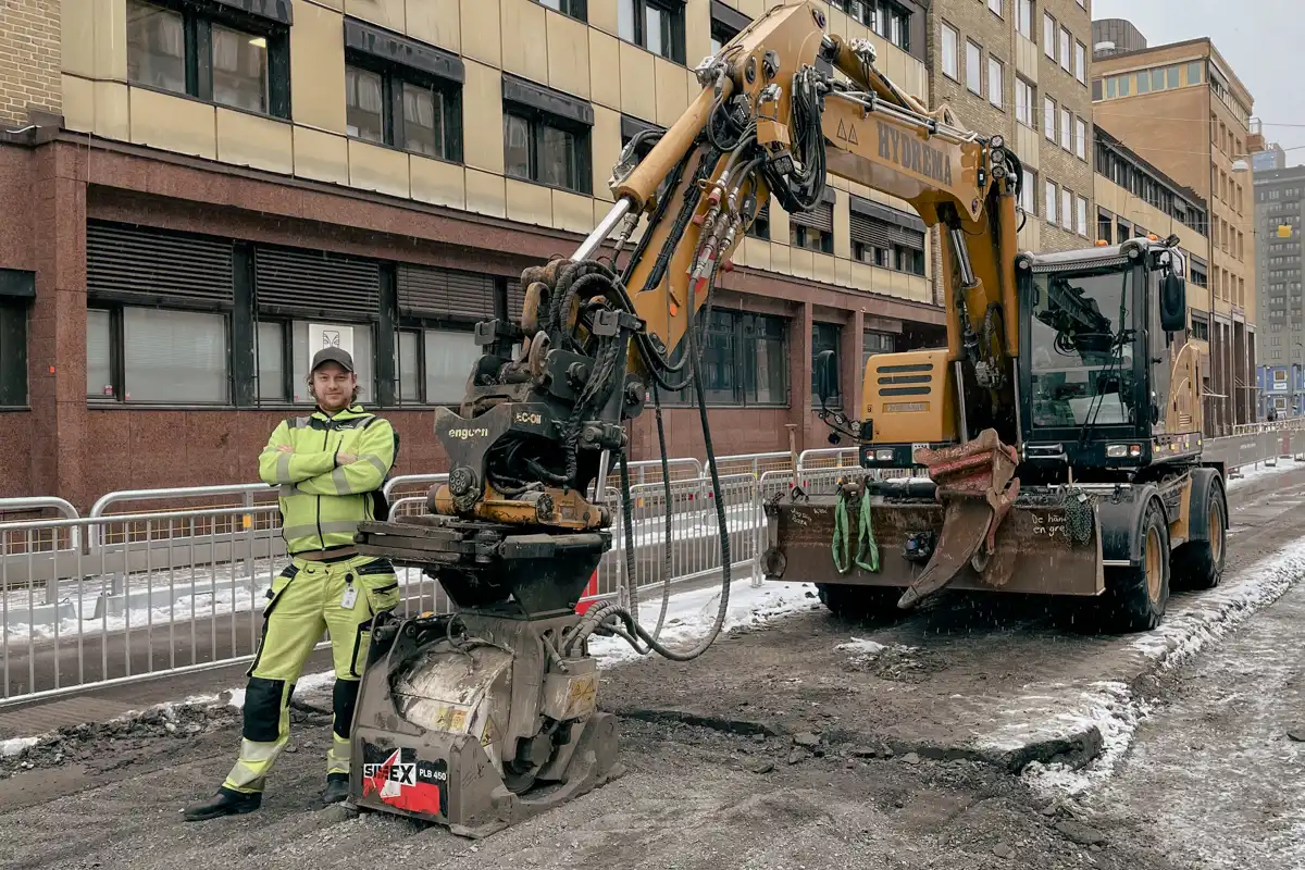 Simex PLB 450 asfaltsfräs på Hydrema-grävare med maskinist stående bredvid under vägarbete.
