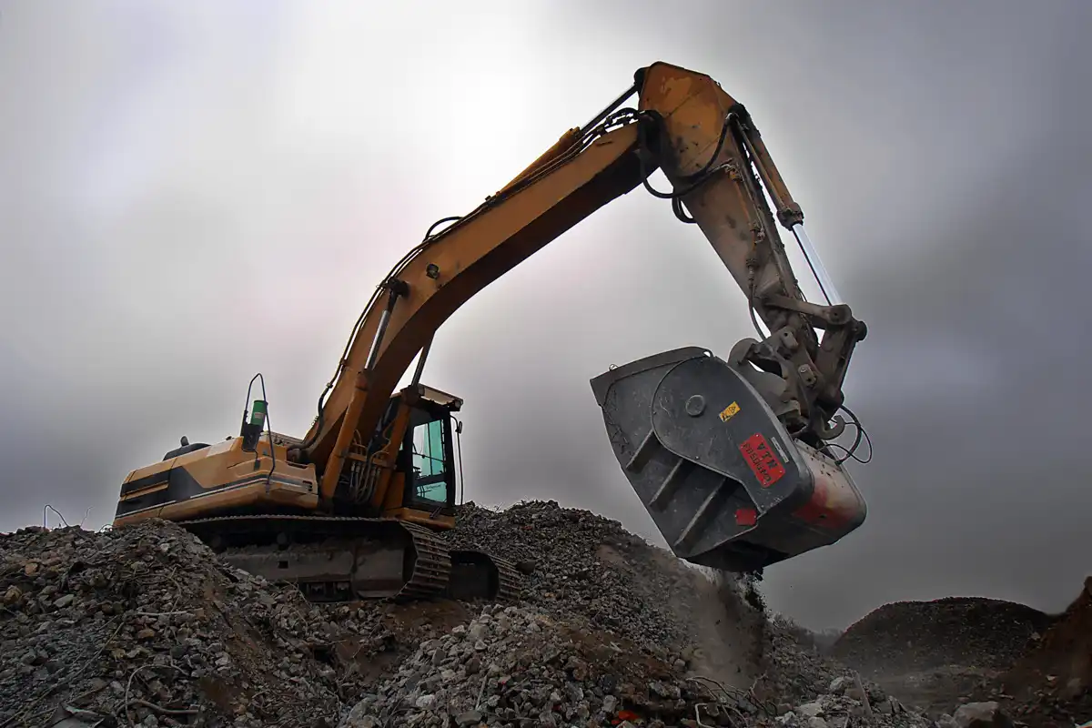 Grävmaskin med VTN krosskopa som krossar betong och asfalt vid rivningsarbete på en återvinningsplats.