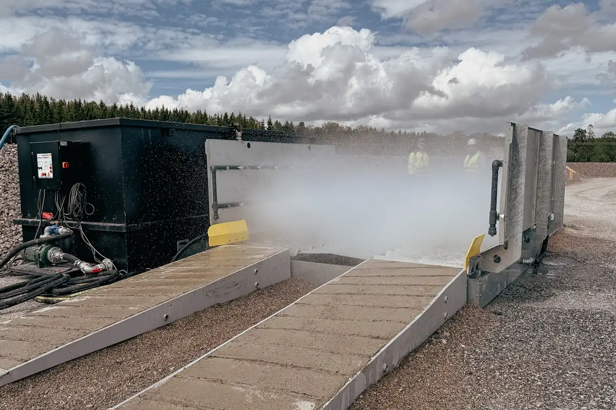 Automatisk hjultvätt på byggarbetsplats som spolar av hjul och chassi innan tunga fordon lämnar området.